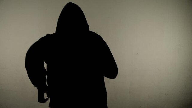 Silhouette of a man in a hoodie running away from the camera against a wall.