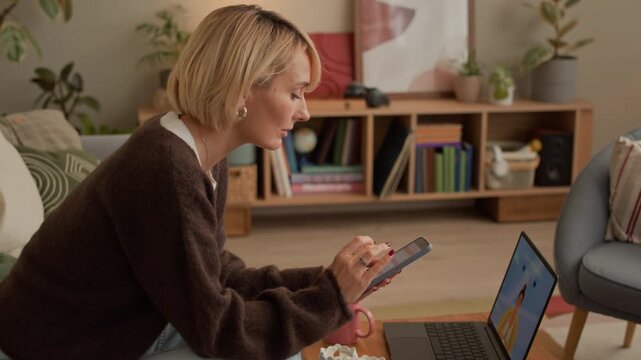Arc shot of adult Caucasian woman checking pregnancy test and using smartphone while meditating with application on wireless laptop at home