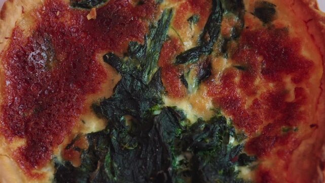 Extreme close view of spinach and cheese quiche with caramelized top and visible leafy greens, rich baked texture and flaky crust forming savory food backdrop