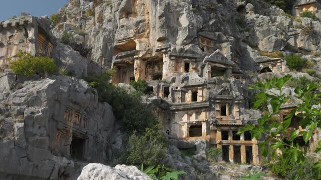 Ancient rock-cut tombs of Myra in Turkey carved into the limestone cliff, detailed view of the Lycian necropolis at daylight. Historic Lycian tombs and architecture in Myra, Turkey. Gimbal shot