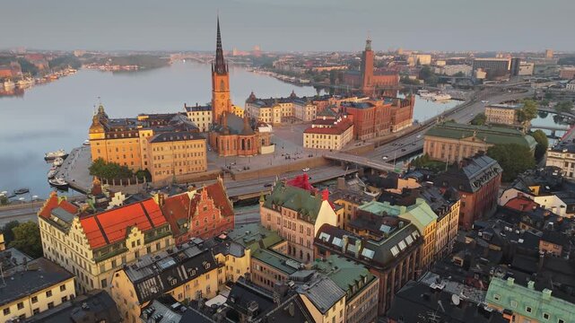 Aerial view of Stockholm old town at sunrise, the camera flies over rooftops towards Riddarholmen church. Scenic morning panorama shows the Swedish capital and calm water. Stockholm, Sweden