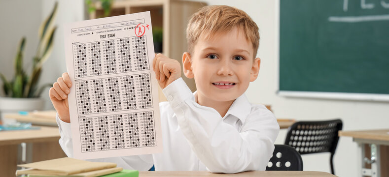 Cute schoolboy with results of test at table in classroom