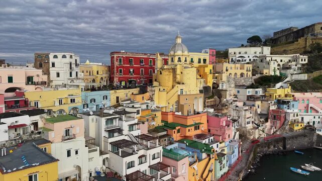 Aerial view shows colorful houses in Corricella harbor on Procida island, beautiful architecture is visible. Local boats are docked in the Mediterranean water. Italian island Procida, Naples