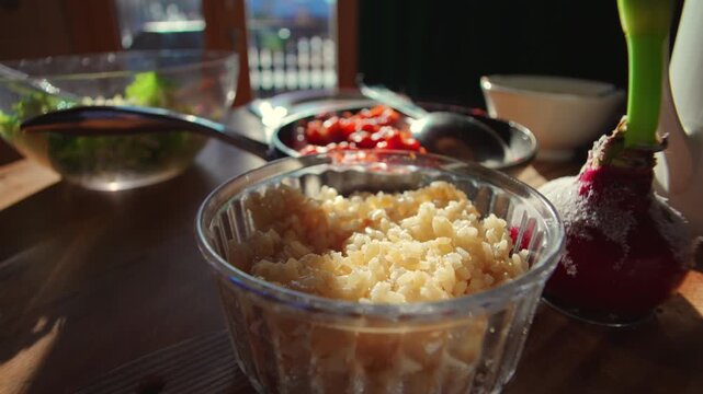 Glass bowl of cooked rice on wooden table inside alpine chalet kitchen, fresh family meal prepared with salad and tomato dish