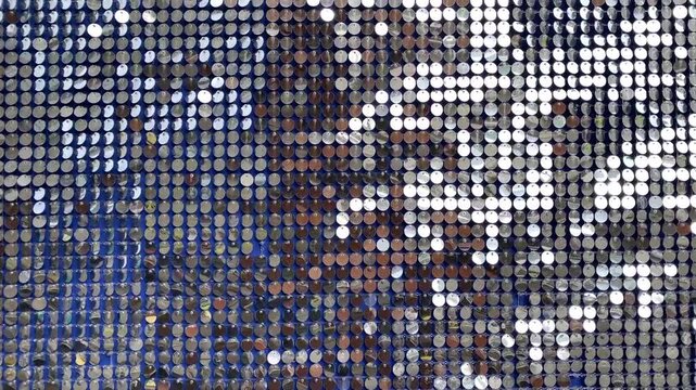 Decorative panel of silver metal discs creating sparkling abstract pattern. Kinetic art installation with moving reflective elements and bokeh lights