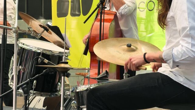 Close-up of a drummer's hands hitting the drum during a live performance. Musicians play on an outdoor stage.