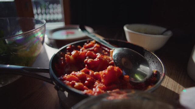 Pan with rich tomato and vegetable stew on wooden table inside alpine chalet kitchen, spoon resting in homemade rustic meal