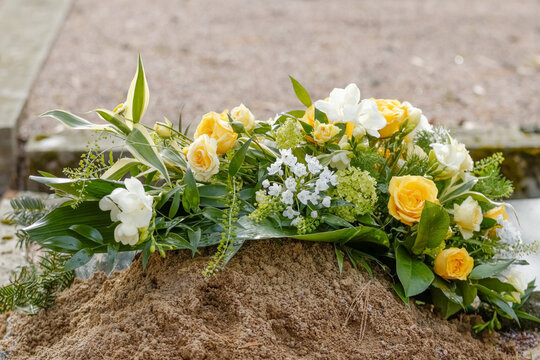 The final resting place. Flower arrangement on an urn grave. Yellow roses and white and green flowers in the cemetery. A beautiful bouquet of memorial flowers. 