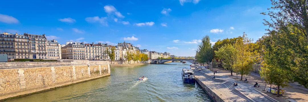 A scenic view of the Seine river looking toward the historic bridges and urban architecture of central Paris with a boat cruising
