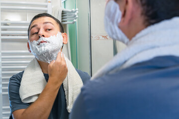 Man smoothing shaving cream while viewing reflection in mirror
