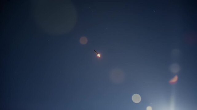 Rocket ascends against deep blue sky, lens flare obscures the background
