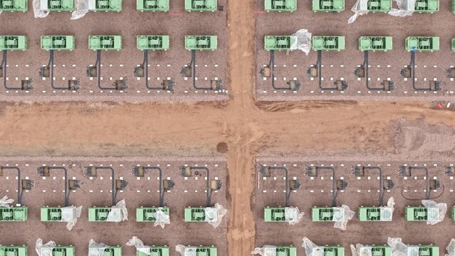 Aerial view of rows of Battery Energy Storage Systems BESS at the National Grid Hams Hall Substation, a juxtaposition of industrial precision against the raw earth, Birmingham, United Kingdom.