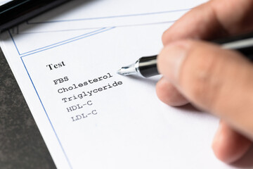 Doctor reviewing cholesterol blood test report with pen during health check examination