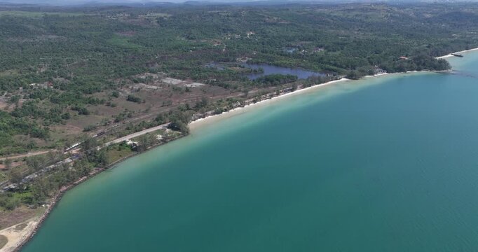 Forward aerial fuel tanker train on tracks parallel to a coastal road, white sand beach, and turquoise water.