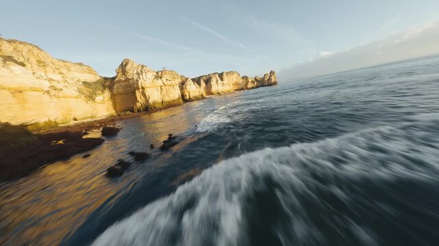 Aerial FPV view of Algarve's golden cliffs meet the turquoise sea in a blur of motion and natural beauty, Algarve, Faro District, Portugal.