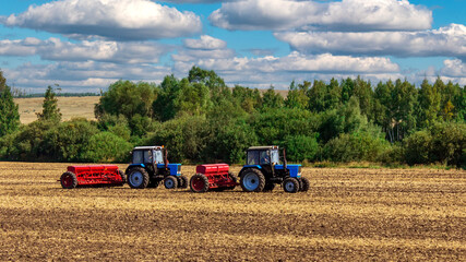 Obraz premium Two tractors are doing sowing or harvesting in the field.