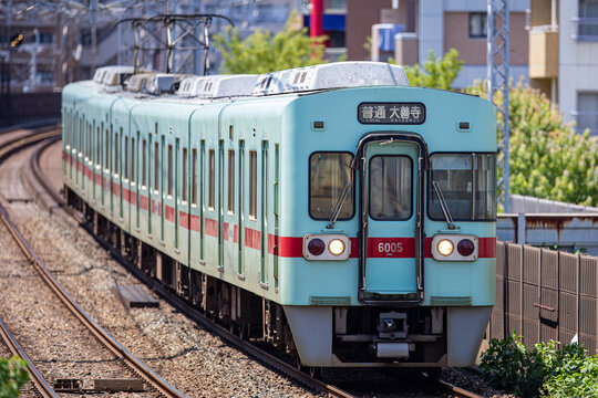 Fukuoka, Japan - 2025 June 28: A Nishi-Nippon Railroad (Nishitetsu) 6000 series train runs on the track. The local train features a traditional ice green body with a red stripe.