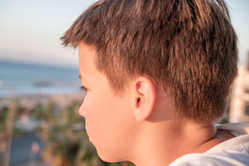 Obraz premium young preteen boy gazing ocean horizon from balcony, golden hour, serene moment contemplation against coastal backdrop, quiet reflection seaside, childhood vacation memory, nature discovery moment
