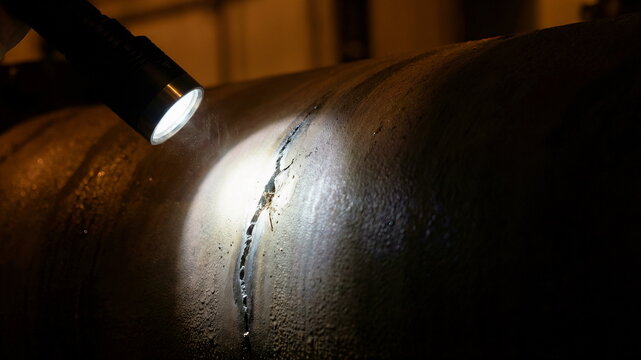 Flashlight illuminates a critical crack in a dark industrial pipe weld, highlighting inspection for maintenance, safety, and quality control.