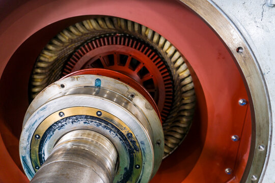 Industrial turbine interior reveals intricate mechanical precision. Metal gears and shafts show advanced engineering design. Red casing contrasts with polished metallic surfaces