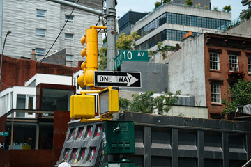 New York City street intersection at 10th Avenue and West 23rd Street with a yellow traffic light and one way sign in an urban Manhattan neighborhood. Modern and historic buildings rise in the