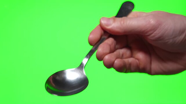 Metal tablespoon in hand on green background
