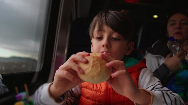 Young Boy Eating Bread Roll by Train Window While Traveling With Family Showing Casual Snack Time and Modern Mobility