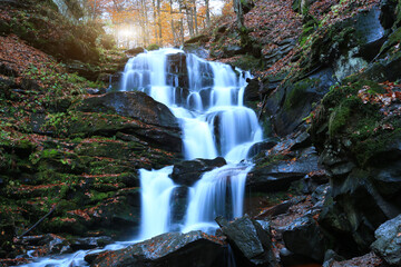 Serene forest waterfall cascades over mossy rocks surrounded by autumn foliage and dappled sunlight © Pavlo Klymenko