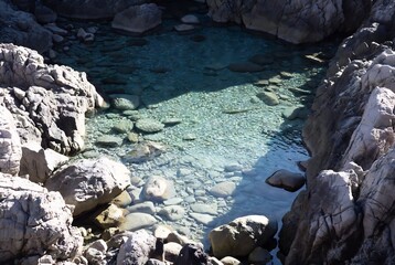 A turquoise pool of water sits nestled among jagged rocks and boulders.