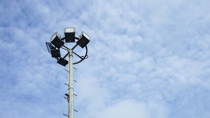 Stadium floodlight pole against a bright blue cloudy sky.