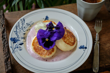  Traditional cottage cheese pancakes syrniki with blackberry cream sauce and purple pansy flowers on a vintage plate.