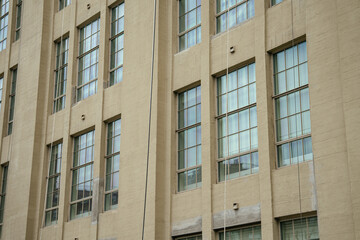 Fototapeta premium A vertical view of a beige architectural facade shows repeating tall windows on a Manhattan building. The clean geometric pattern highlights modern urban design and city structure in New York.