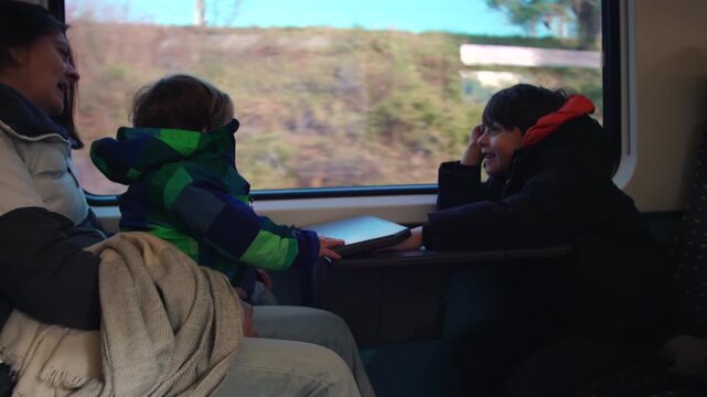 Mother traveling by train with two sons seated at cabin table, family watching passing scenery through window during relaxed rail journey together