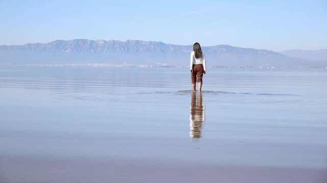 Beautiful visual of a woman walking through very shallow water that creates a perfect reflection of the sky in Ebro Delta, Tarragona, Spain.