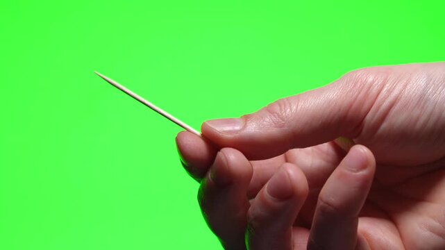 A person holding a wooden toothpick on a green isolated background.
Dental hygiene and health