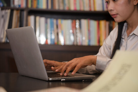 Asian woman working on laptop in library. Happy female successfully completes the thesis report and passed final exam. Education Concept.