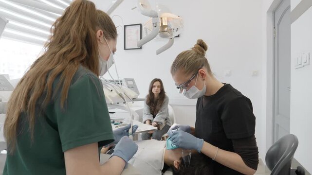 Female dentist uses small applicator brush to apply protective fissure sealant or fluoride varnish on teenage boy patient teeth for caries prevention during family dental clinic visit.