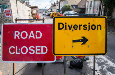 Obraz premium Red Road Closed sign beside yellow Diversion arrow sign on a roadside. Traffic management concept, transport disruption and temporary direction signage.