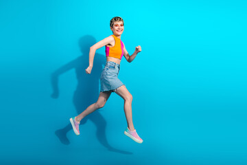 Obraz premium Young woman jumps in colorful top and denim skirt against blue background for a vibrant fashion lifestyle stock photo
