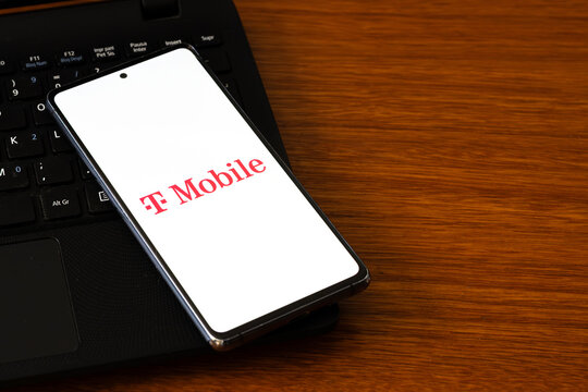 Punta Arenas, Chile &ndash; March 05, 2026: A smartphone screen displaying the T-Mobile telecommunications logo, resting on a black laptop keyboard over a wooden desk surface