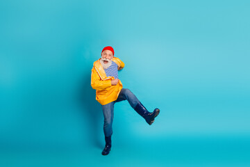 Obraz premium Senior man in orange raincoat jumping with joy against blue background for stock photo