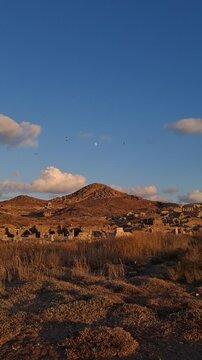 Scenic view of Delos island featuring ancient Greek ruins, standing columns, scattered marble blocks illuminated by warm summer light. Greece, Mediterranean travel
