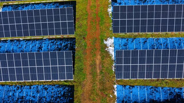 Top down view of solar panels and dirt path. Aerial shot showing symmetry of solar modules separated by a brown ground access road and grass.