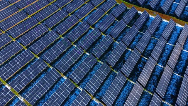 Diagonal rows of solar panels on winter ground. High angle view of photovoltaic panels arranged in diagonal lines across a field with patches of snow.