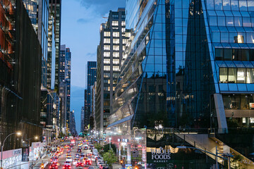 Fototapeta premium New York City, New York, USA - 08.02.2024: Evening traffic moves through Hudson Yards in Manhattan with illuminated glass skyscrapers and Whole Foods Market visible. The night city scene captures
