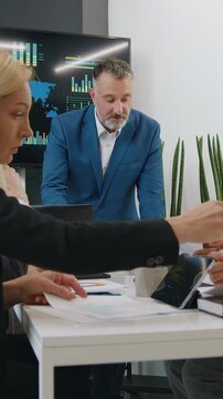 Likable multiracial team man and woman of analytics sitting at boardroom table and discussing financial documents while handsome successful serious bearded director holding a meeting