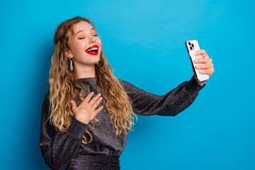 Joyful girl in a shiny dress takes a selfie against blue background showcasing glamour confidence...