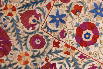 Fototapeta premium Intricate colorful wall embroidery on a traditional textile featuring hand-stitched Uzbek floral motifs, swirling vines and ornamental patterns. Close-up detail highlights texture and craftsmanship