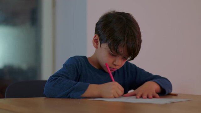 Young boy writing answers on homework worksheet at table concentrating on school assignment and carefully completing academic task during evening study time