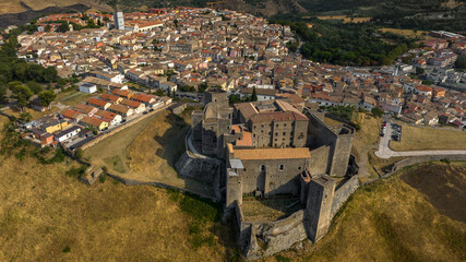 Aerial view of Melfi, a town in Basilicata, Southern Italy. It's a historic city featuring a large stone castle on a grassy hill overlooking a dense network of houses and narrow winding streets. © Stefano Tammaro